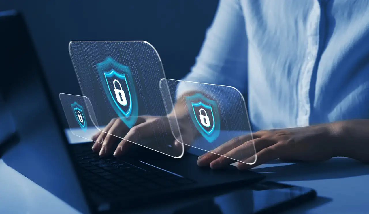 Computer user typing while holographic security shields float above laptop keyboard.